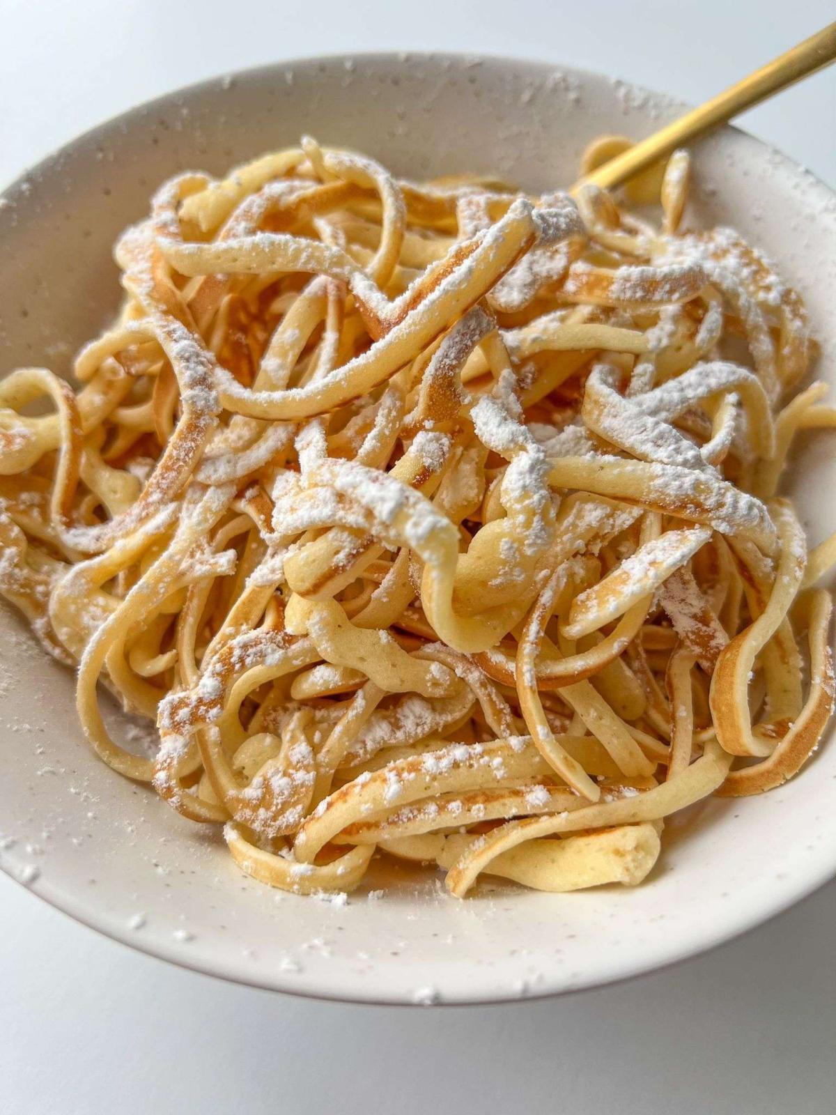 pancakes in the shape of spaghetti with powered sugar on top in a bowl.